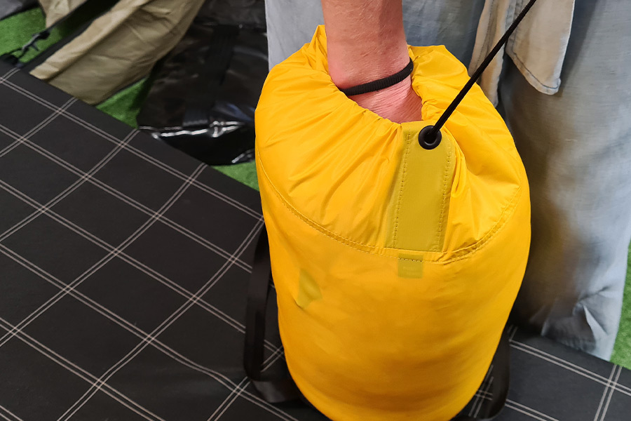 A fist is submerged inside a full sleeping bag compression sack while another hand out of shot pulls the drawstring closed.