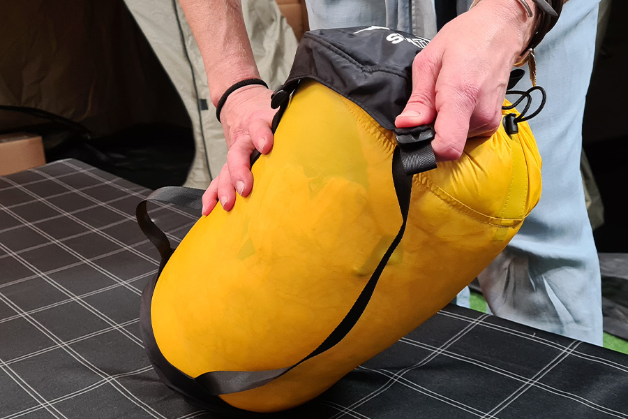 Two hands fit the black cap over the top of a yellow compression sack.
