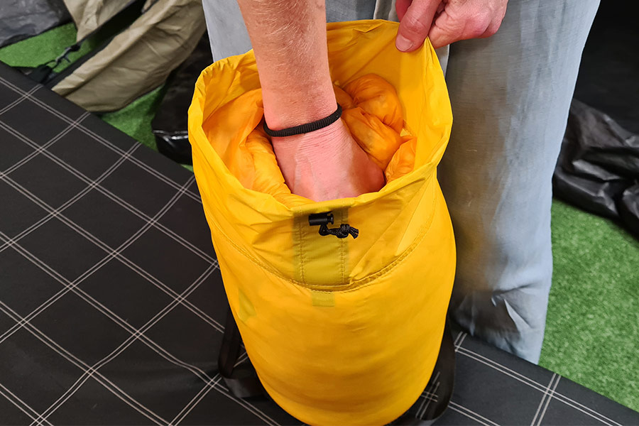 A fist pushing the last of a yellow sleeping bag into a stuff sack. 