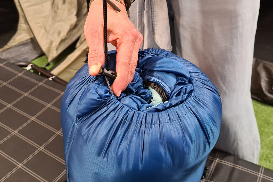 Close up of a hand securing the draw string toggle of a blue compression sack in place.