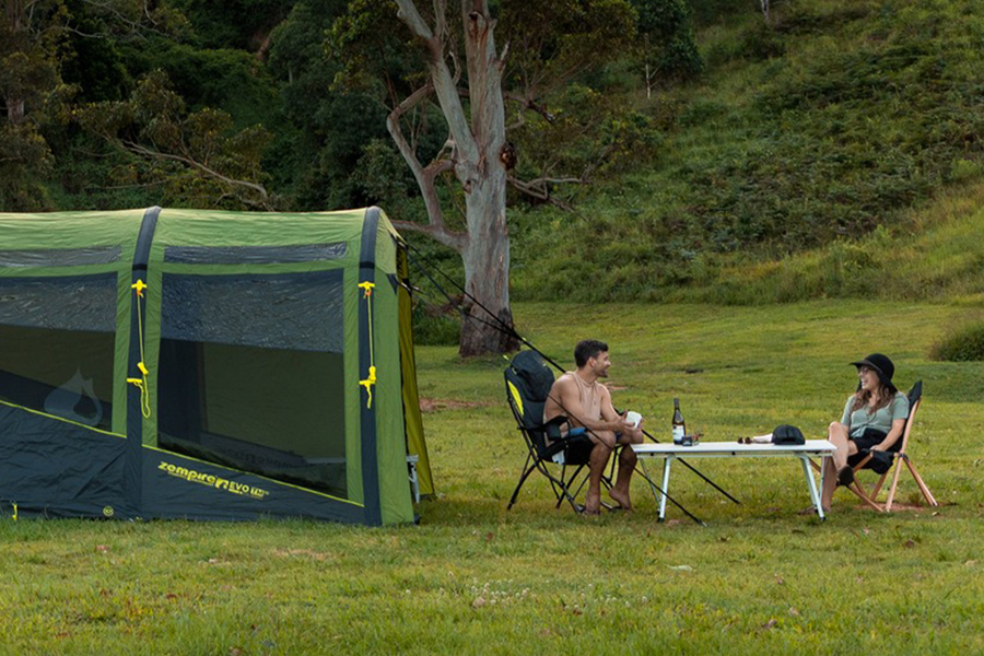 A couple sitting outside their Zempire tent in the great outdoors. 