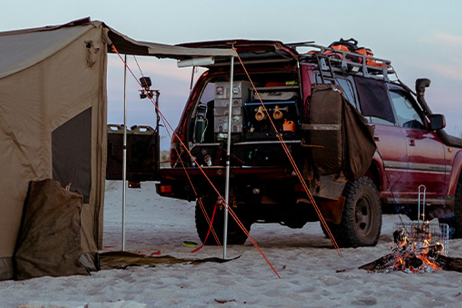 A 4WD beach setup with a campfire at sunset.