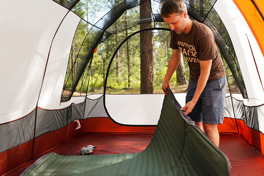 A man with a sleeping mat inside a tent. 